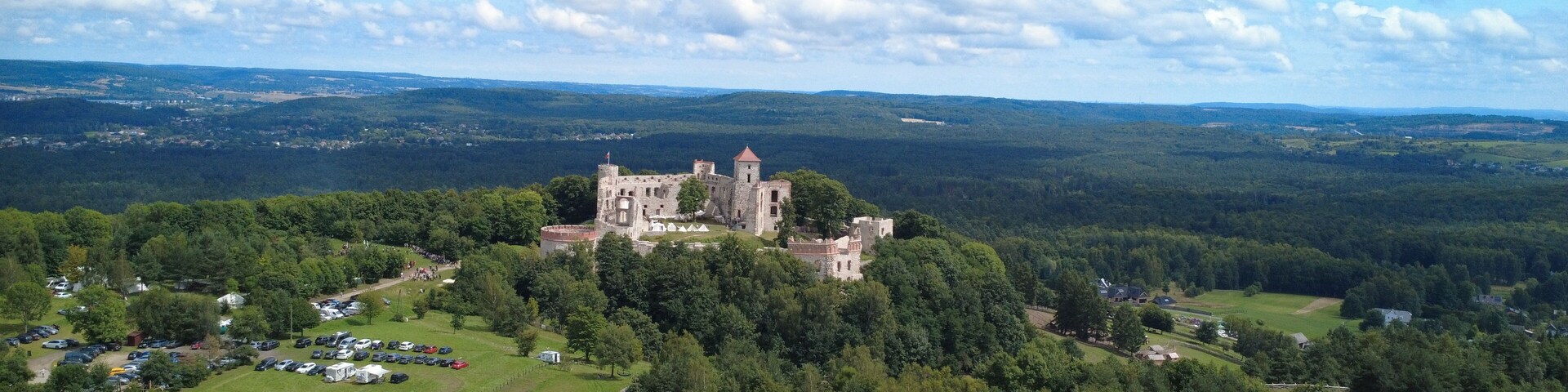 Aerial view of Tenczyn Castle in Rudno, Poland. The medieval ruins are surrounded by lush green forests and rolling hills, creating a stunning contrast between history and nature.