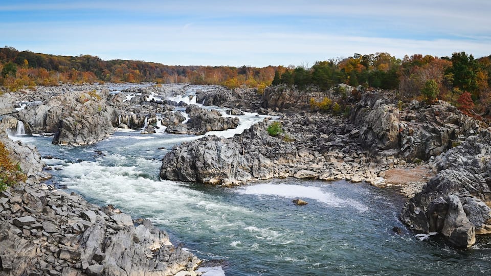A river flowing through a rocky gorge with autumn foliage in the background.