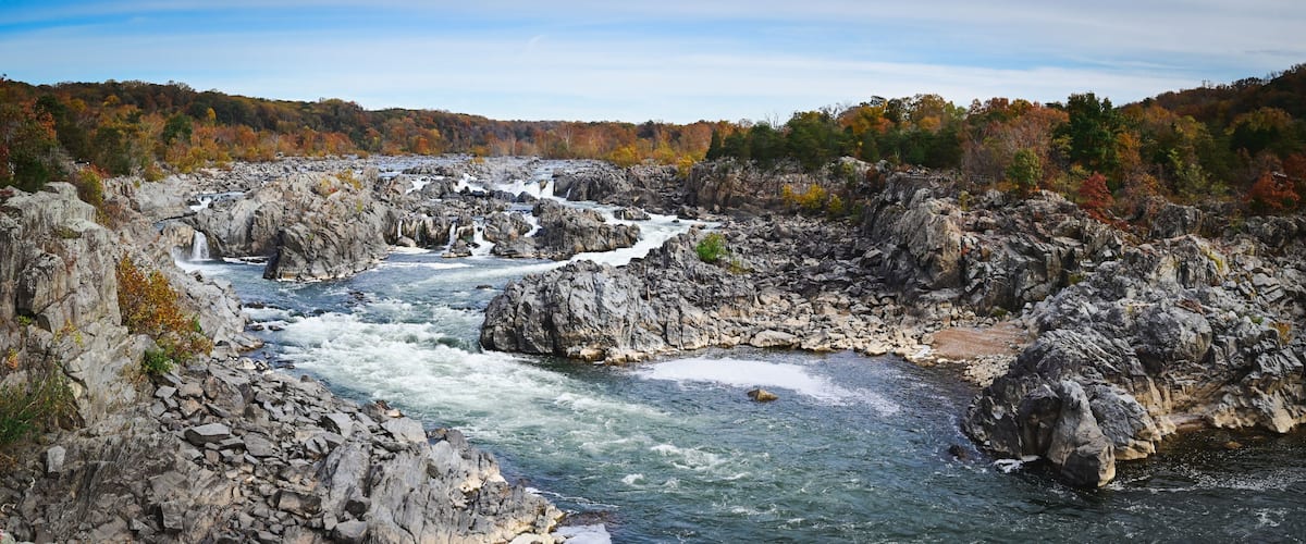 A river flowing through a rocky gorge with autumn foliage in the background.