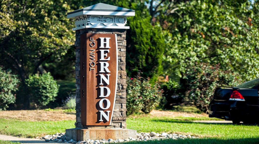 Stone sign for city or town of Herndon in Northern Virginia suburbs by green trees park near Washington DC