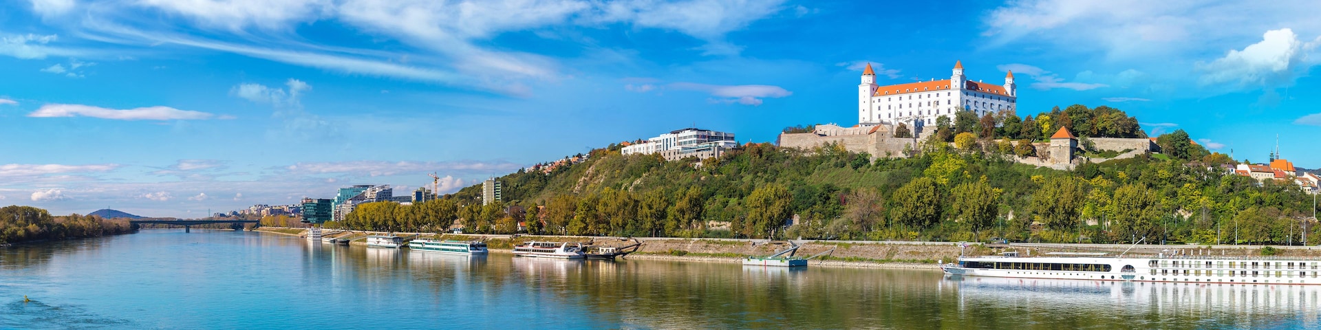 Um castelo no topo de uma colina, com vista para um rio e barcos.