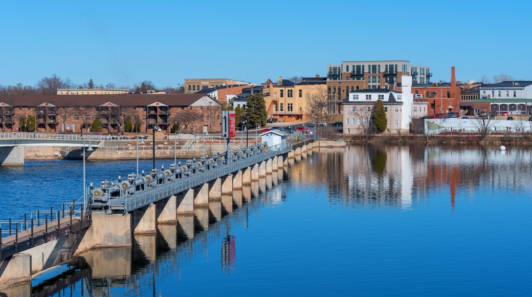 A calm river with a bridge, buildings, and a clear blue sky.