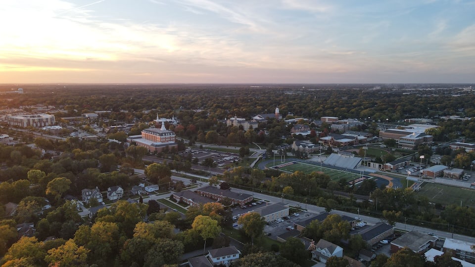 An aerial view of a cityscape with a prominent university campus, various buildings, and surrounding greenery.
