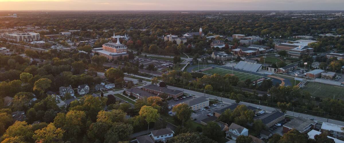 An aerial view of a cityscape with a prominent university campus, various buildings, and surrounding greenery.