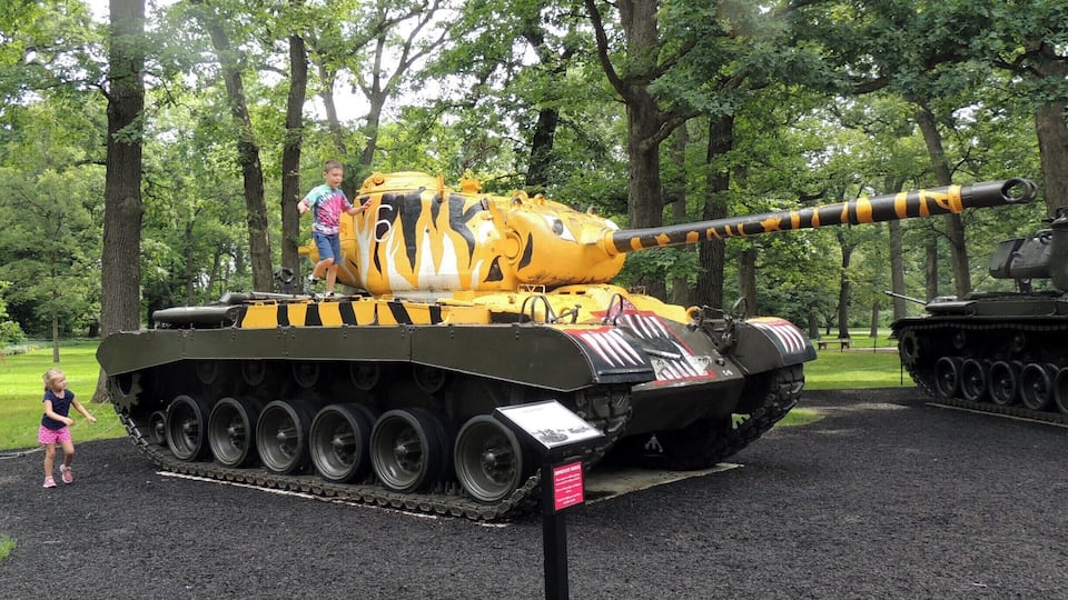 A yellow and black tank with a long barrel, surrounded by trees.