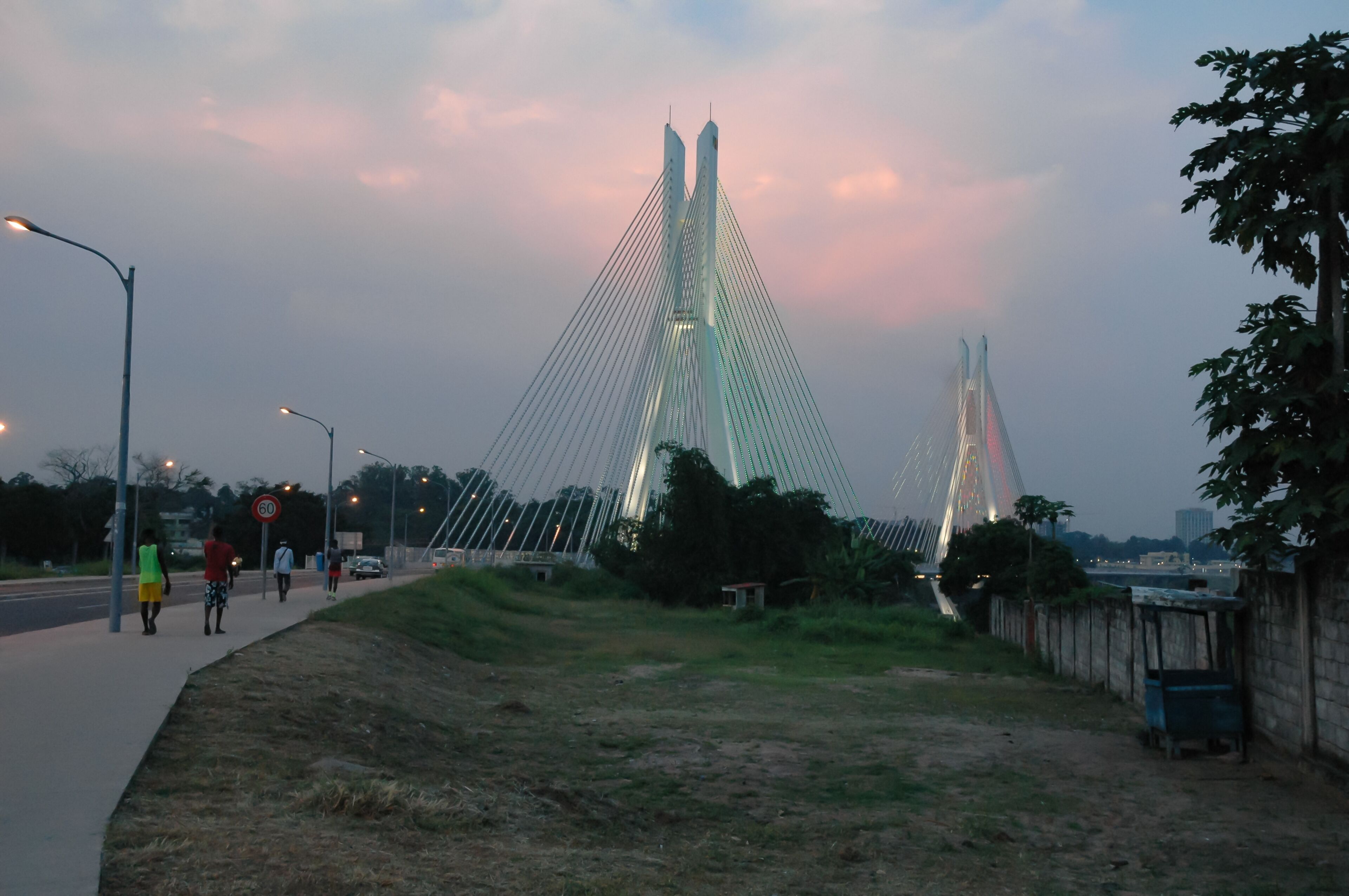 A modern cable-stayed bridge with two towers, a pedestrian walkway, and a grassy area beside the road.