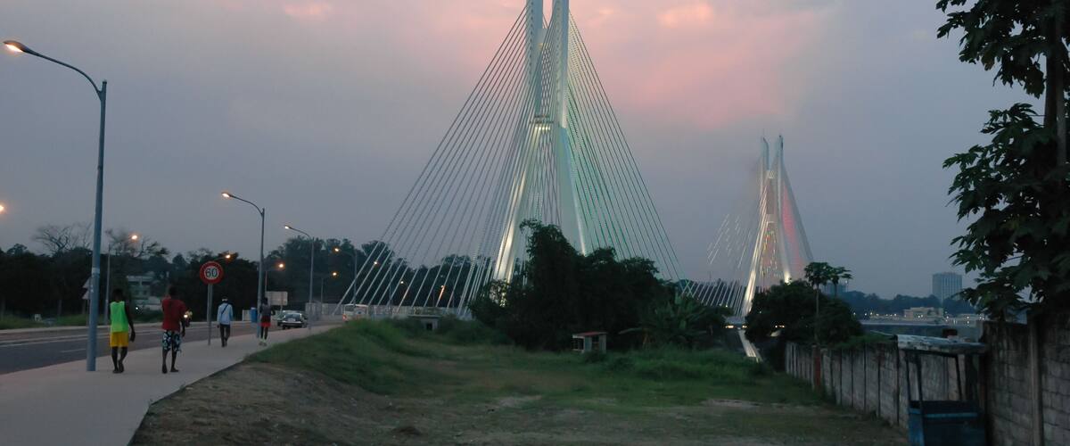 A modern cable-stayed bridge with two towers, a pedestrian walkway, and a grassy area beside the road.