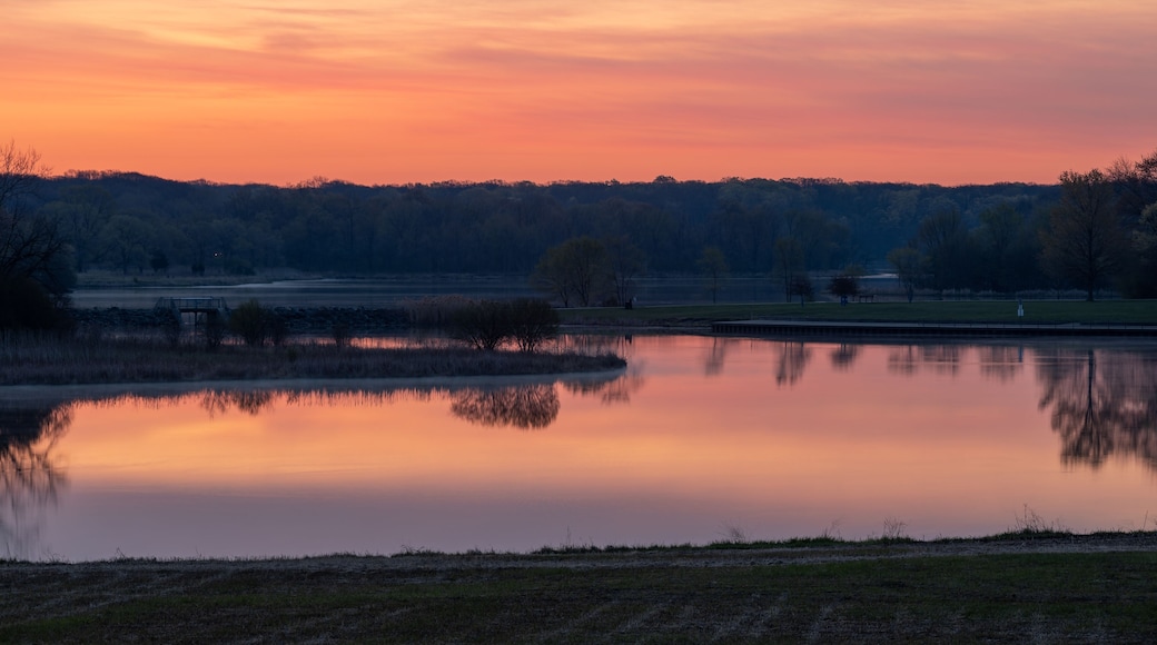 Una puesta de sol serena sobre un lago tranquilo con una colina boscosa al fondo.