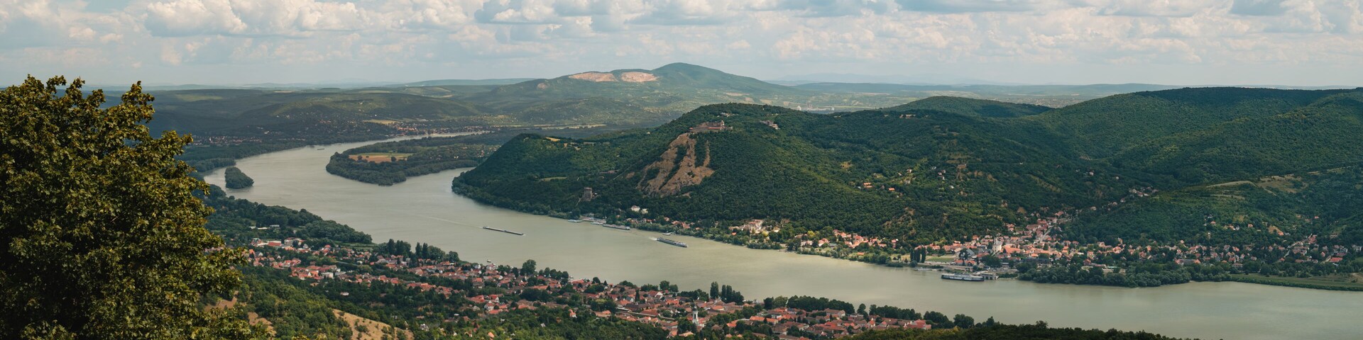 The Danube Bend unfolds in stunning beauty, with Visegrád Castle perched above and Nagymaros resting peacefully along the river’s edge under a bright summer sky