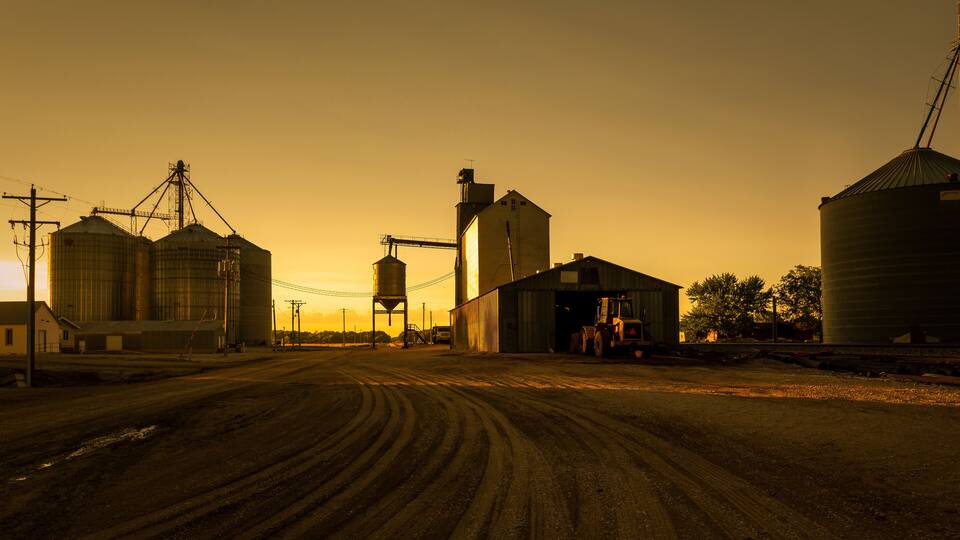 A rural landscape with large grain silos, a dirt road, and a barn.