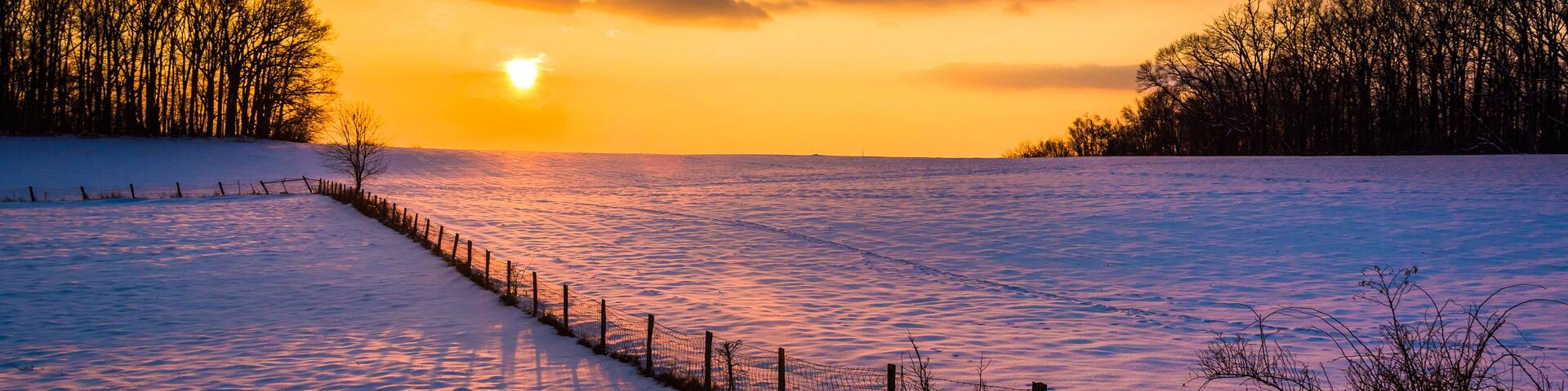 Sunset over a fence in a snow covered farm field in rural Carrol