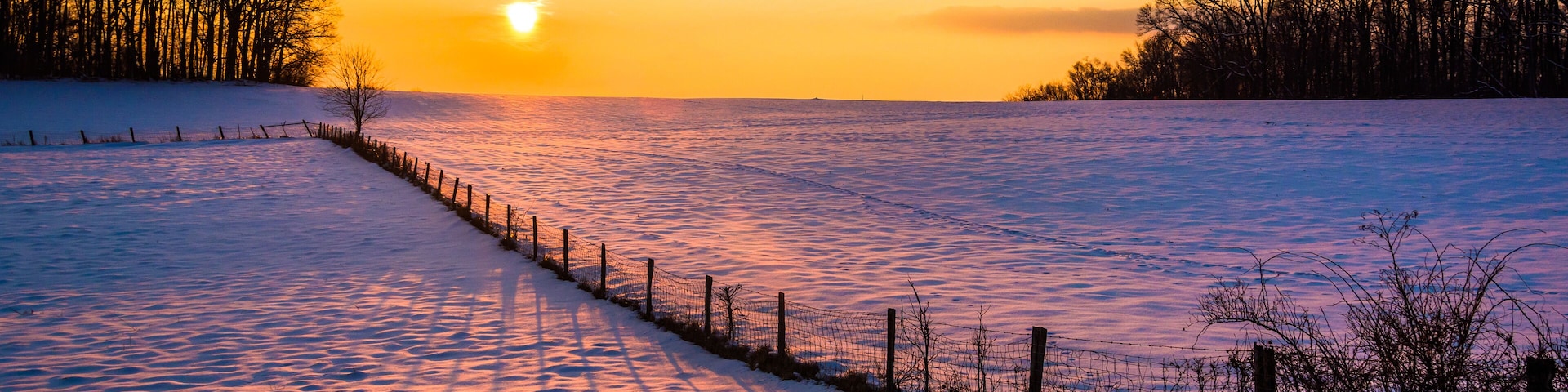 Sunset over a fence in a snow covered farm field in rural Carrol
