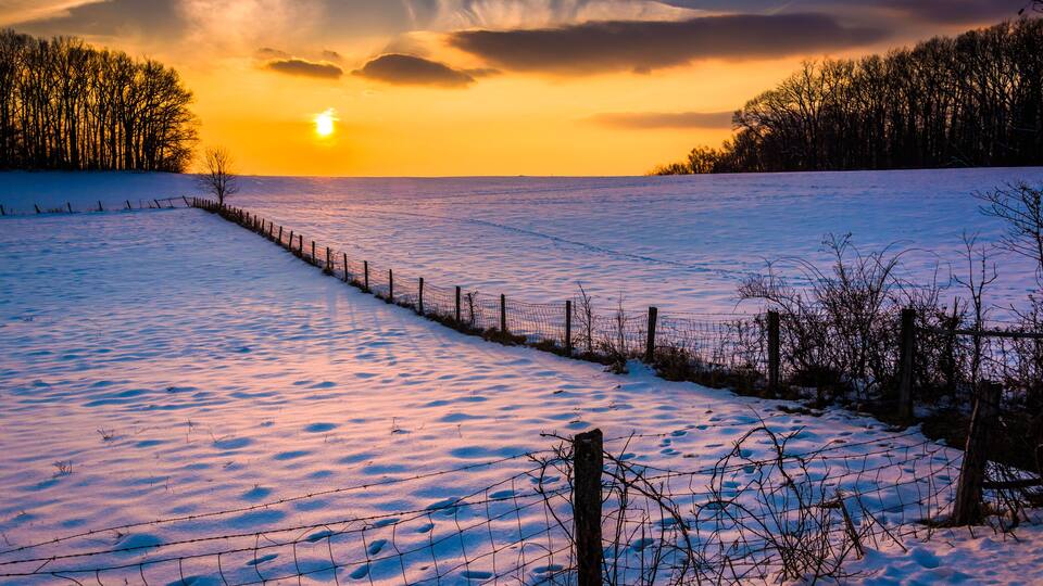 Sunset over a fence in a snow covered farm field in rural Carrol