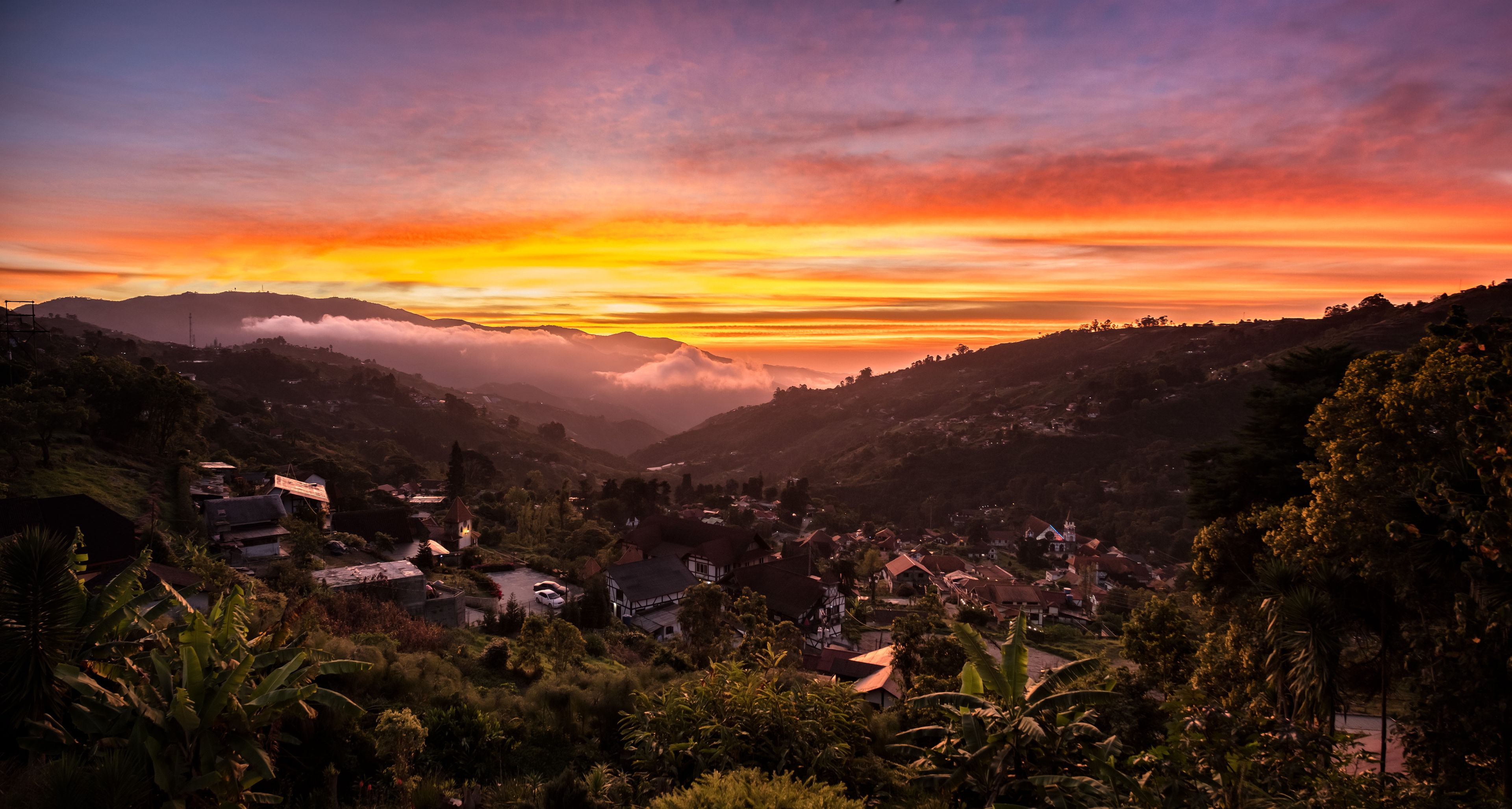 A valley with a sunset, houses, and mountains.