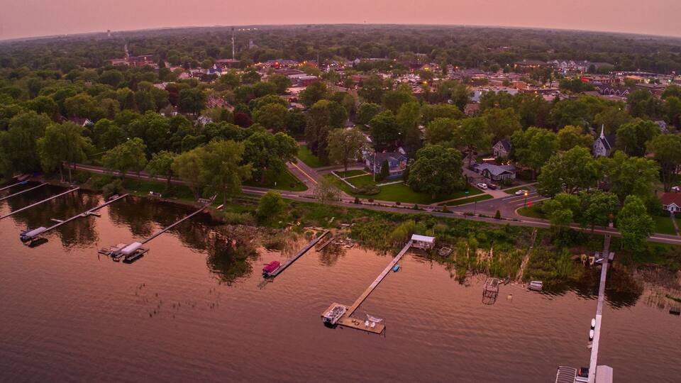 An aerial view of a lakeside community with boats docked, a pier, and surrounding greenery.
