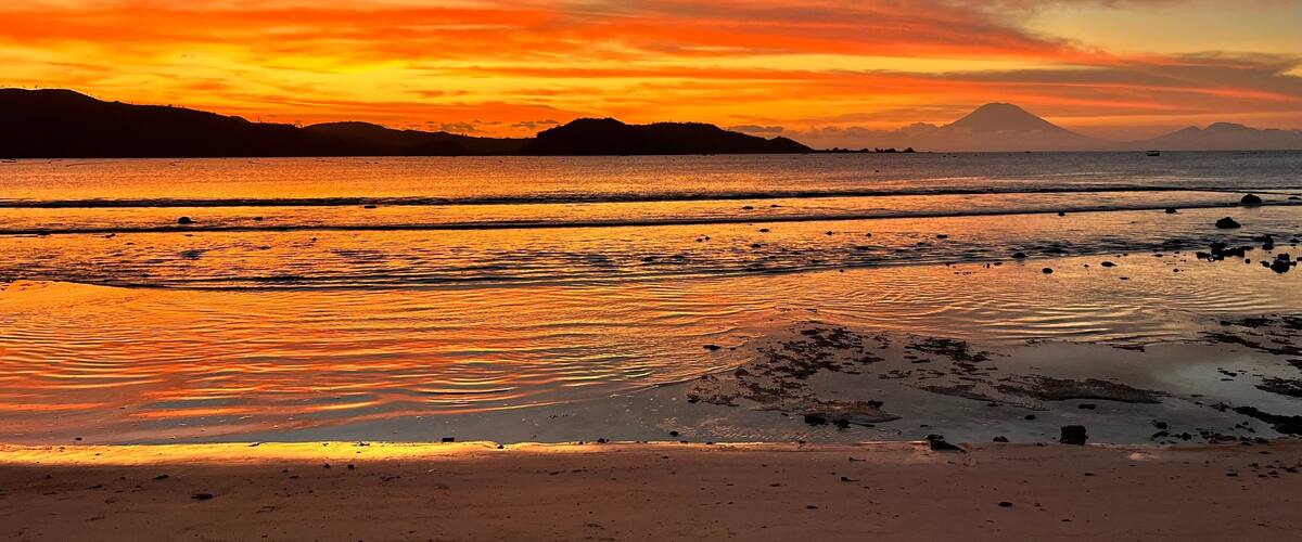 A sunset over a beach with waves reflecting the sky's colors.