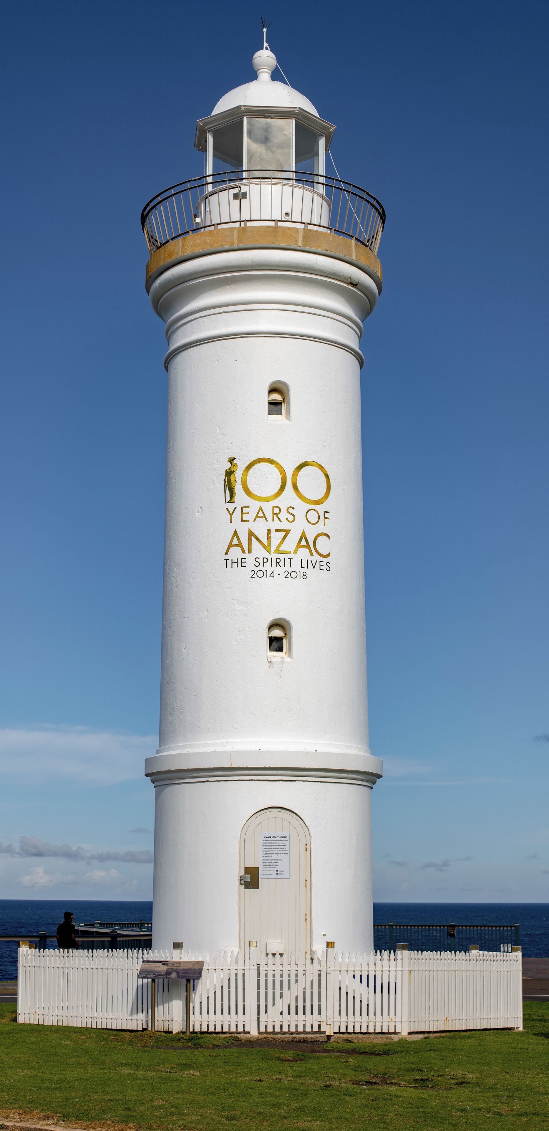 A white lighthouse with a balcony and a fence in front.