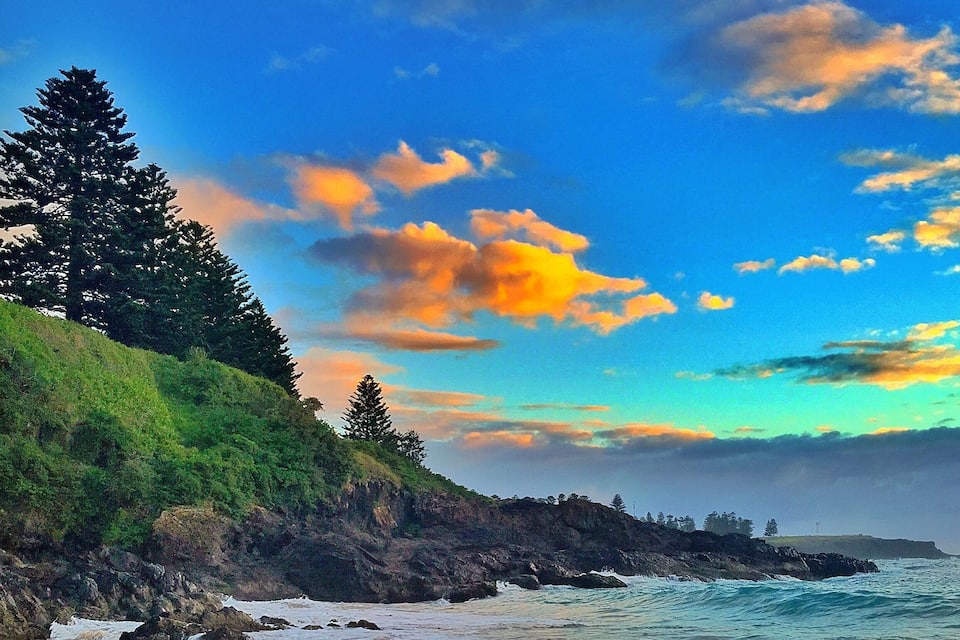 A beach with waves, a rocky coastline, and trees.