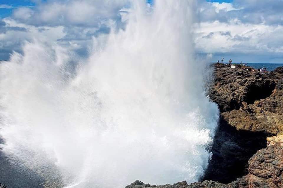 A large water spout at a rocky coastline with people observing.