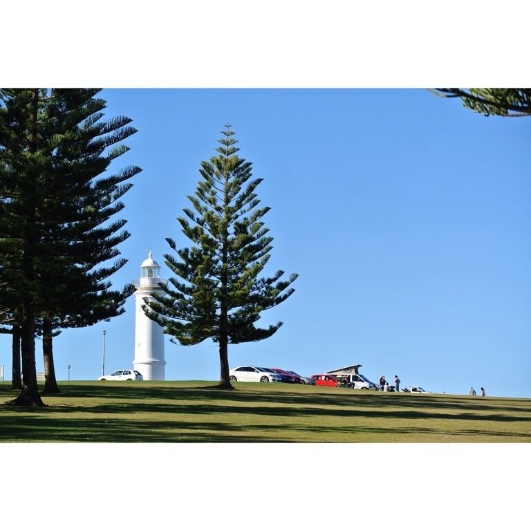 A white lighthouse, a grassy hill, and several cars parked on the hill.