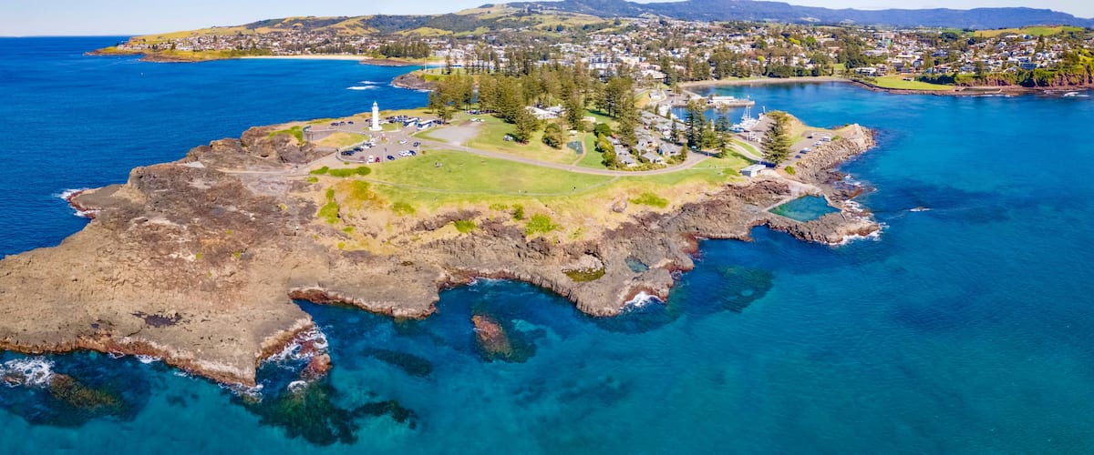 An aerial view of a coastal town with a lighthouse, rocky shoreline, and a marina.