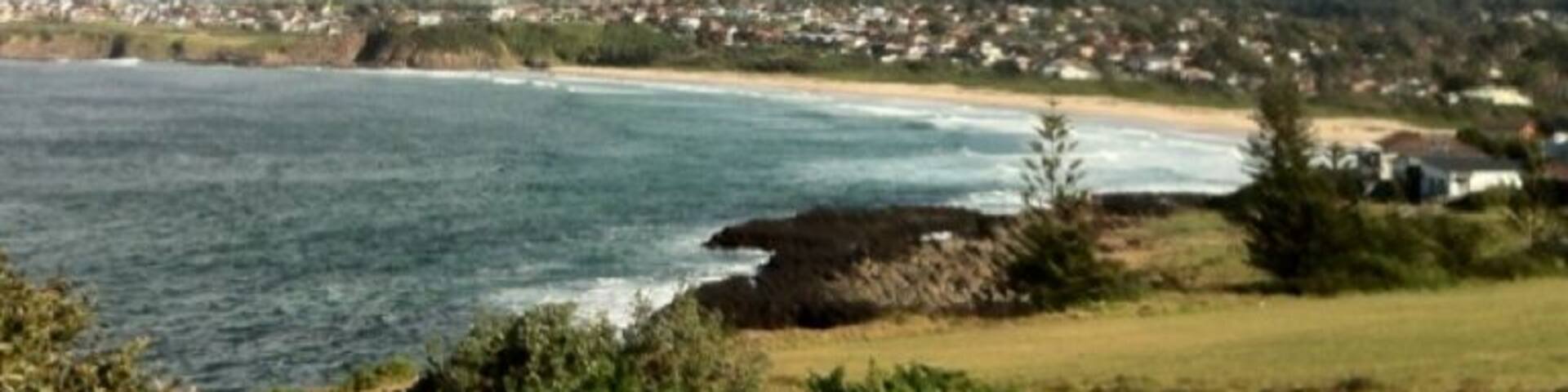 A coastal landscape with a beach, ocean waves, and a town in the background.