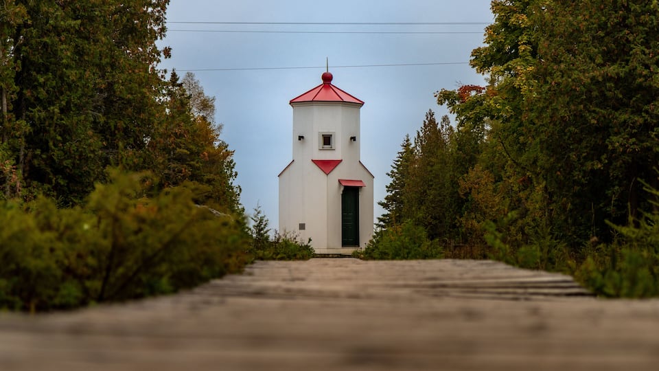 A white church with a red roof and a green door, surrounded by trees.