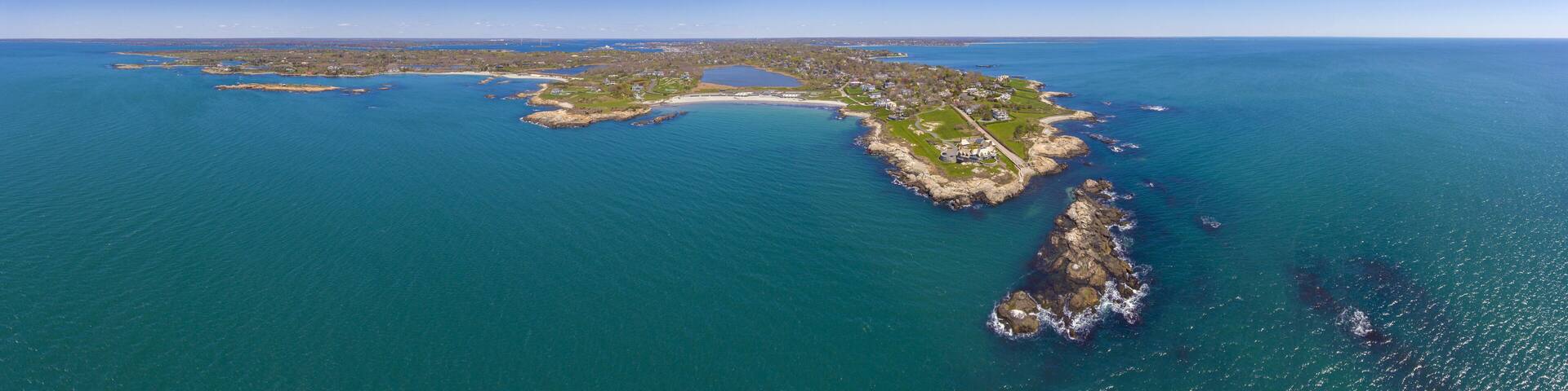 An aerial view of a coastal island with a mix of residential areas, green spaces, and rocky coastlines.