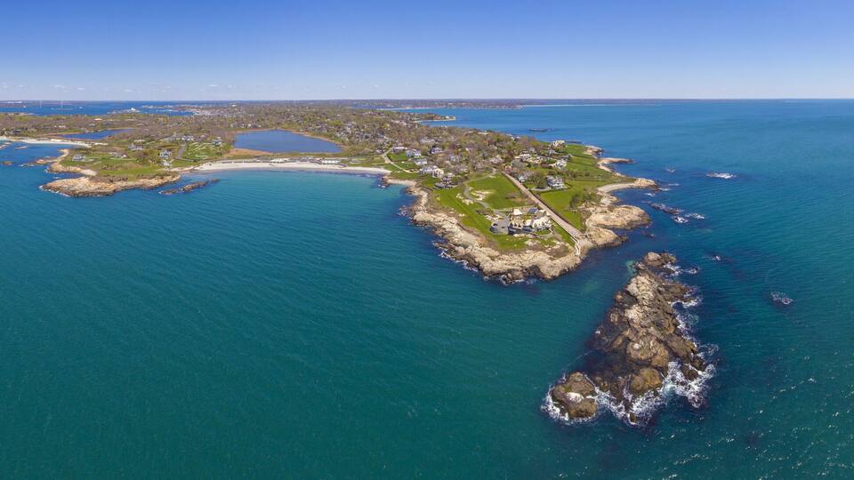 An aerial view of a coastal island with a mix of residential areas, green spaces, and rocky coastlines.