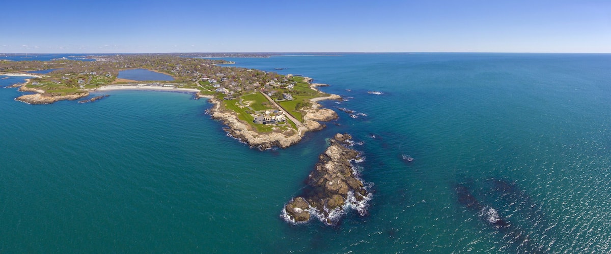 An aerial view of a coastal island with a mix of residential areas, green spaces, and rocky coastlines.