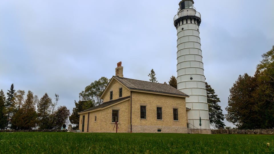 A lighthouse and a small building in a grassy field.