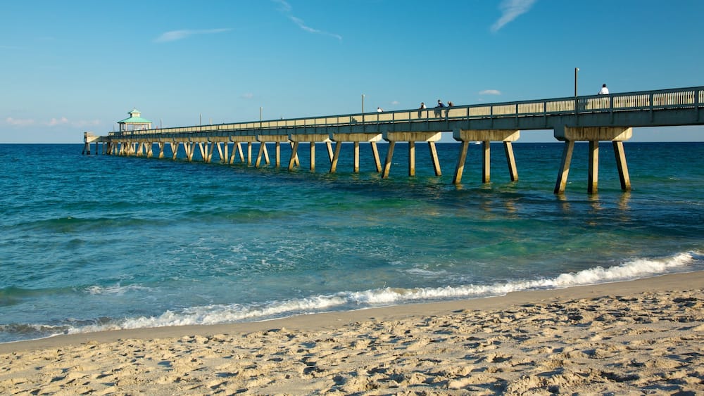 A pier extending into the ocean with clear blue water and a sandy beach.