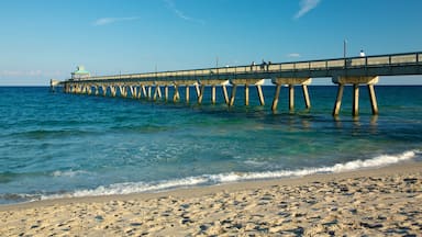 Um píer se estende sobre o oceano, com águas azuis cristalinas e uma praia de areia.