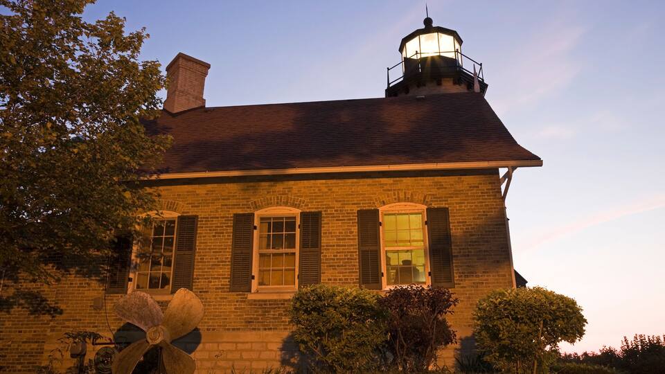 A brick building with a lighthouse on the roof, surrounded by trees and bushes.