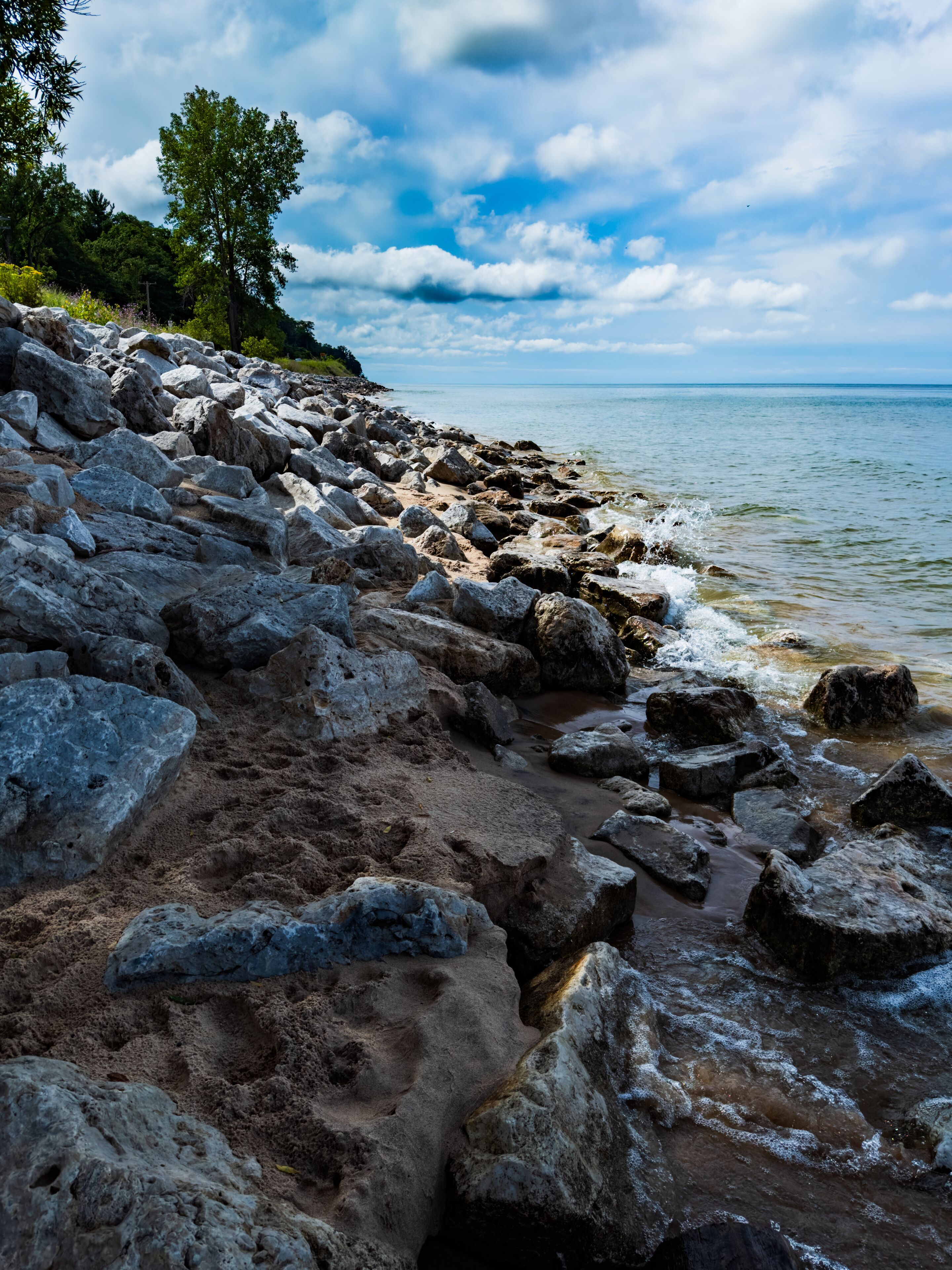 A rocky shoreline with large boulders, a clear sky, and a calm sea.