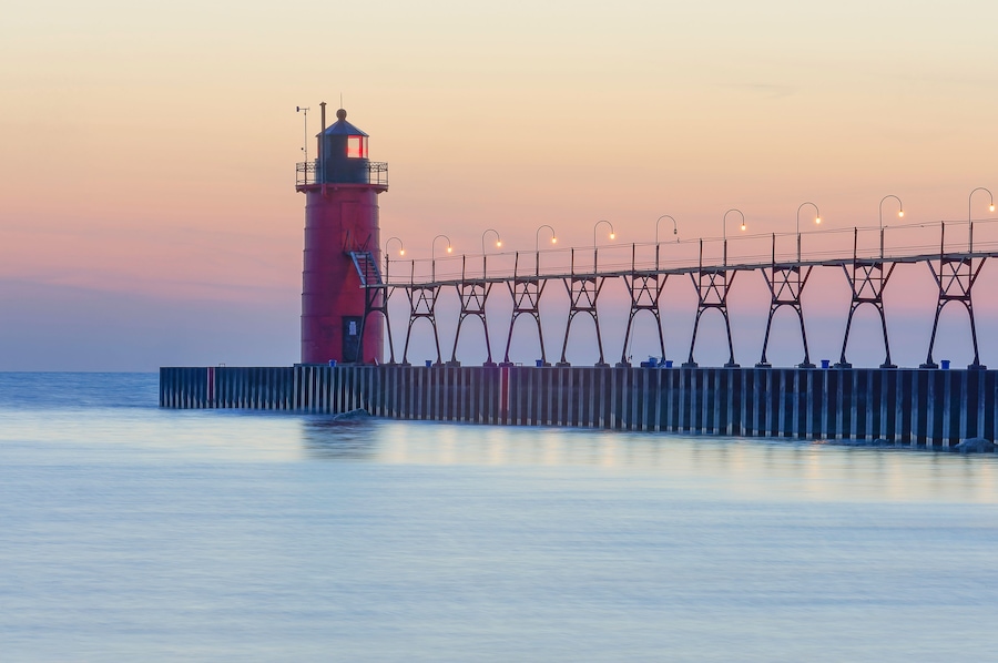 A lighthouse with a red tower and a pier with street lamps.
