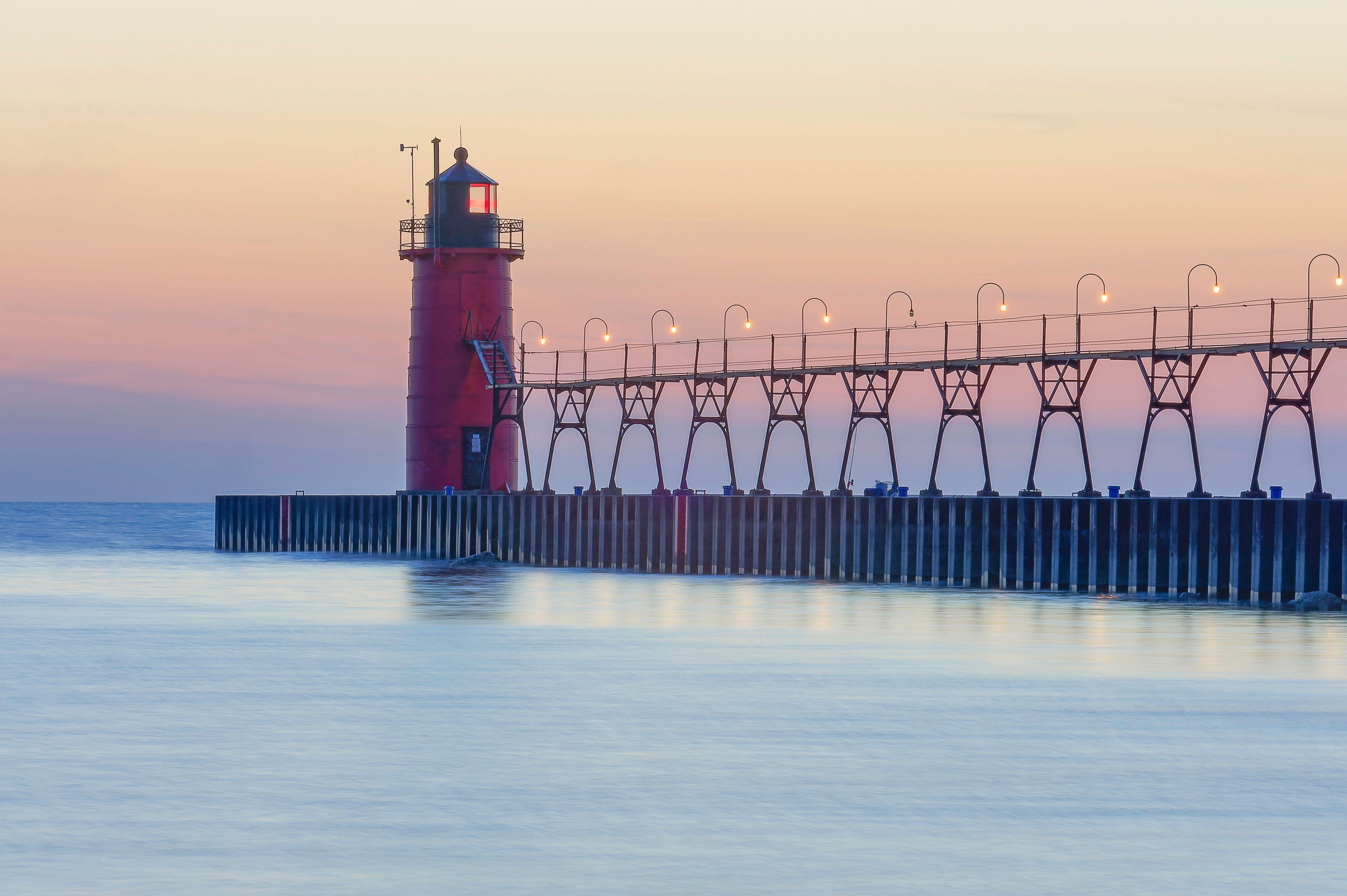 A lighthouse with a red tower and a pier with street lamps.