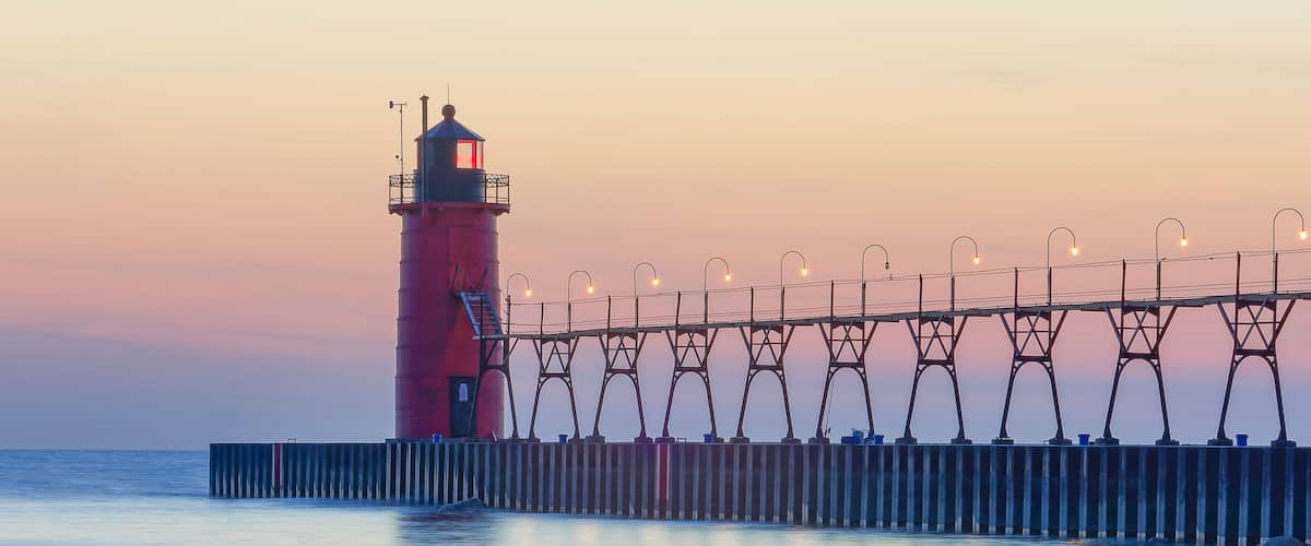 A lighthouse with a red tower and a pier with street lamps.