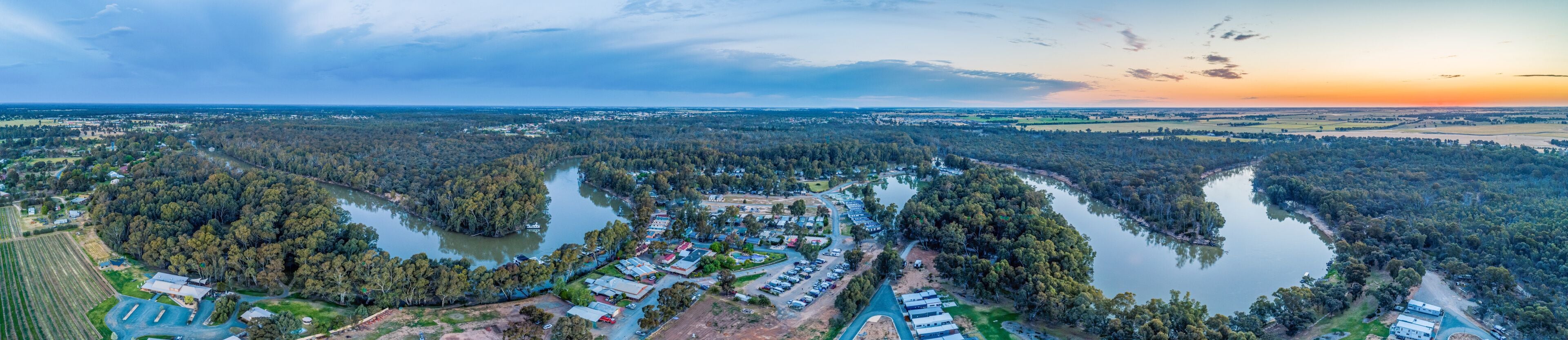 A panoramic view of a lakeside community with dense forests, a river, and residential buildings.
