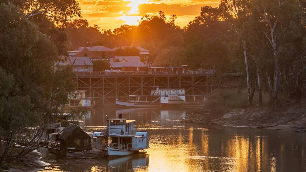 A river with a boat docked near a bridge, surrounded by trees and buildings.