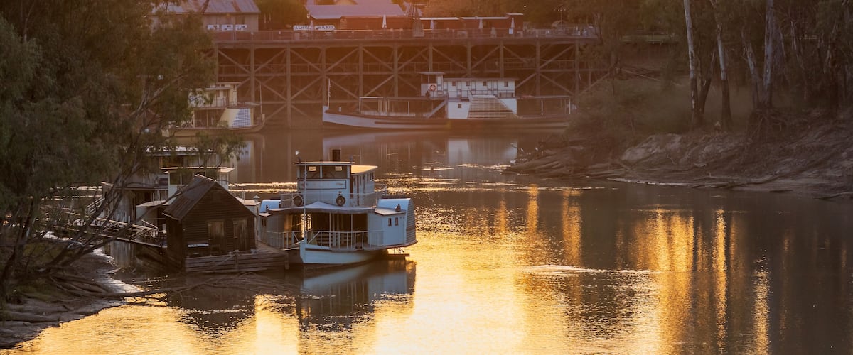 A river with a boat docked near a bridge, surrounded by trees and buildings.
