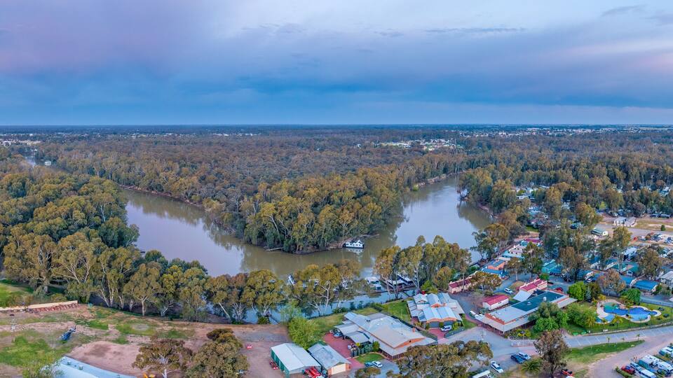 An aerial view of a town with a river, surrounded by dense forests and fields.