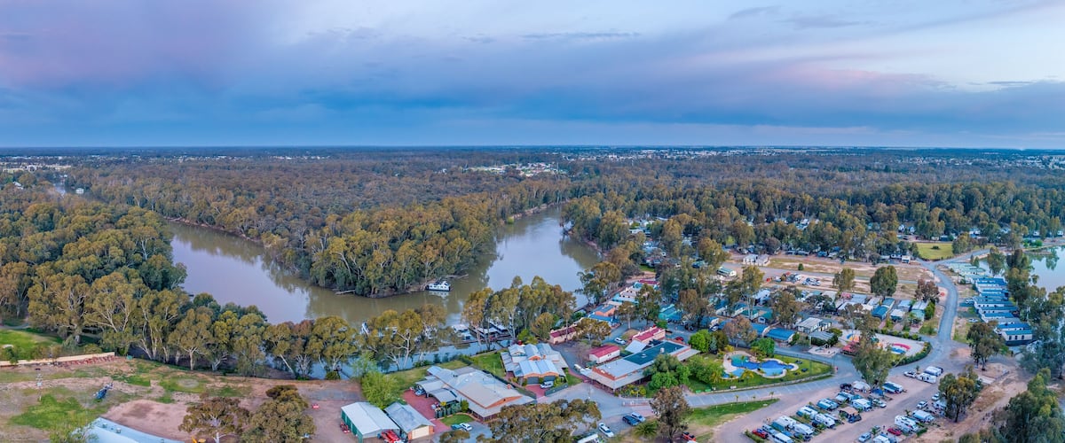 An aerial view of a town with a river, surrounded by dense forests and fields.
