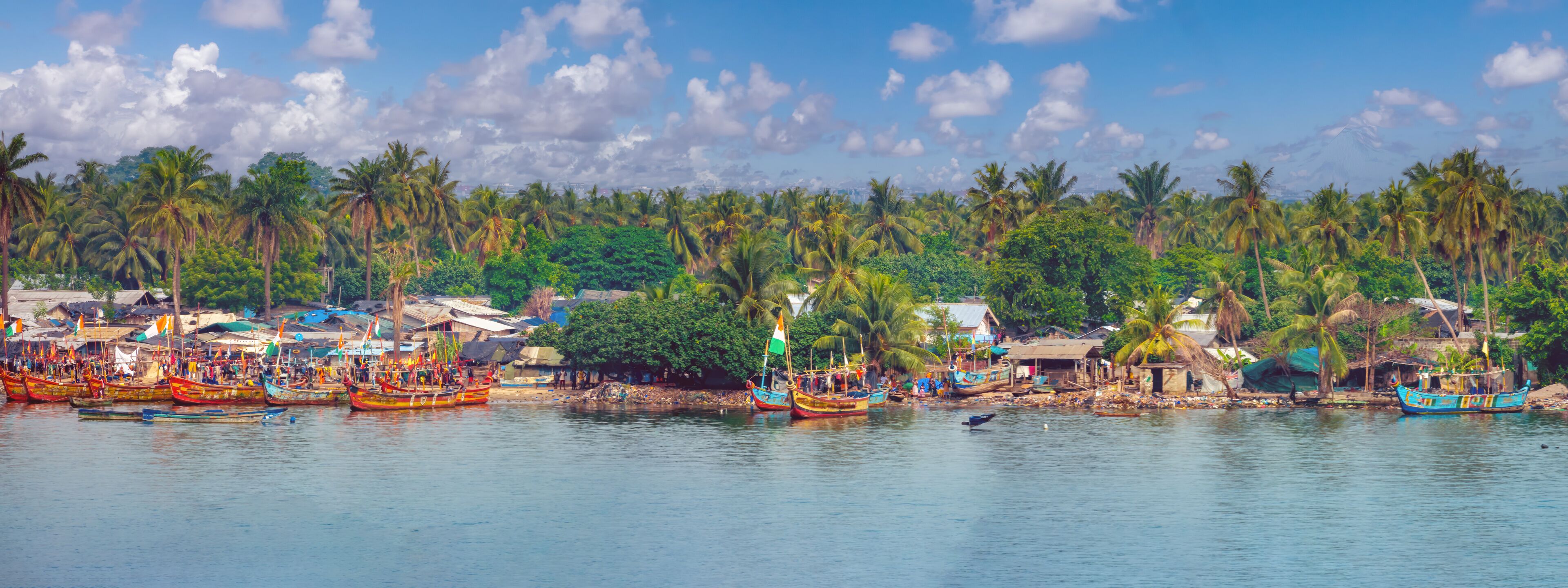 A coastal village with colorful boats docked along the shore, surrounded by lush palm trees and traditional huts.
