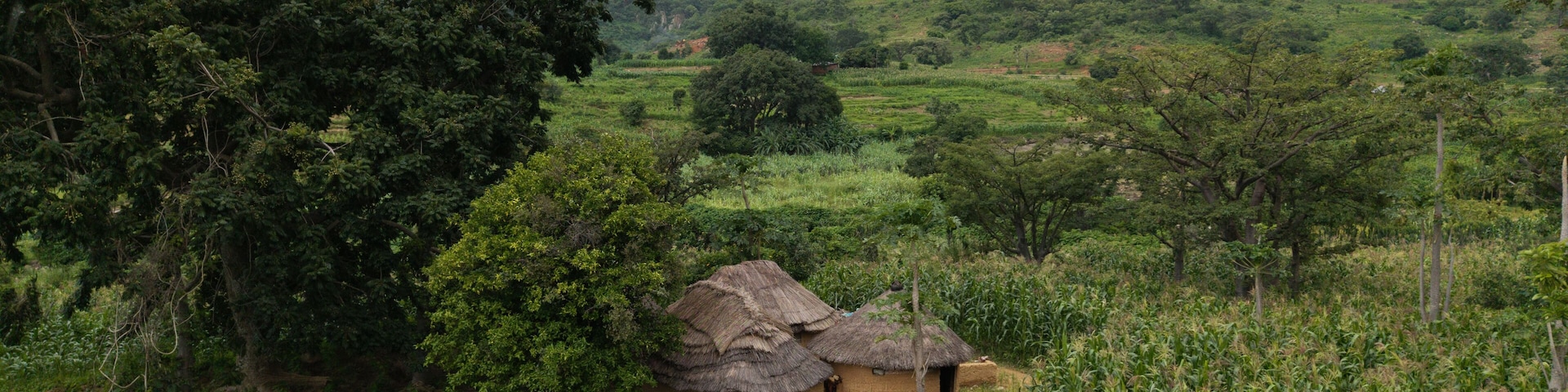 Aerial view of thatched huts nestled amongst verdant fields, backed by rolling hills under a cloudy sky, Jos, Jos North, Nigeria.