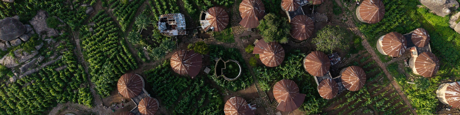 Aerial view of clusters of round, thatched-roof huts nestled amidst lush green fields, creating a textured tapestry from above, Jos, Plateau, Nigeria.