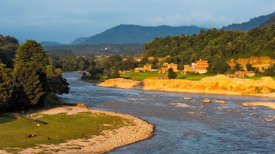 A river flowing through a valley with a temple and lush greenery.
