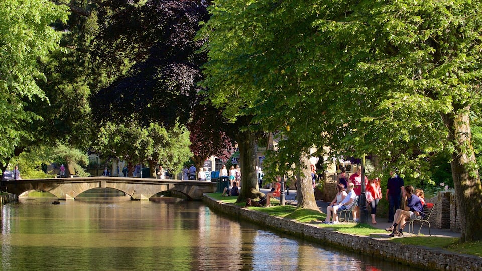 A stone bridge over a calm river, surrounded by lush green trees and a stone wall.
