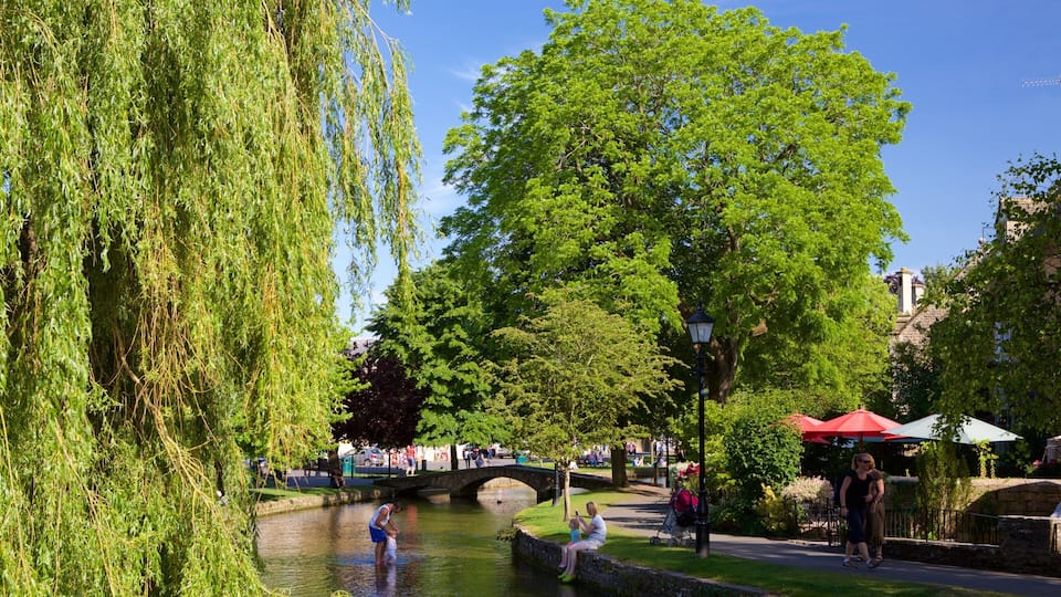A river with a stone bridge, lush greenery, and people enjoying the outdoors.