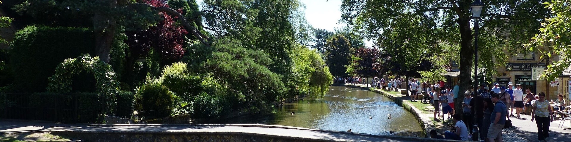 Ein Park mit Teich, Enten, einer Steinbrücke und Spaziergängern.